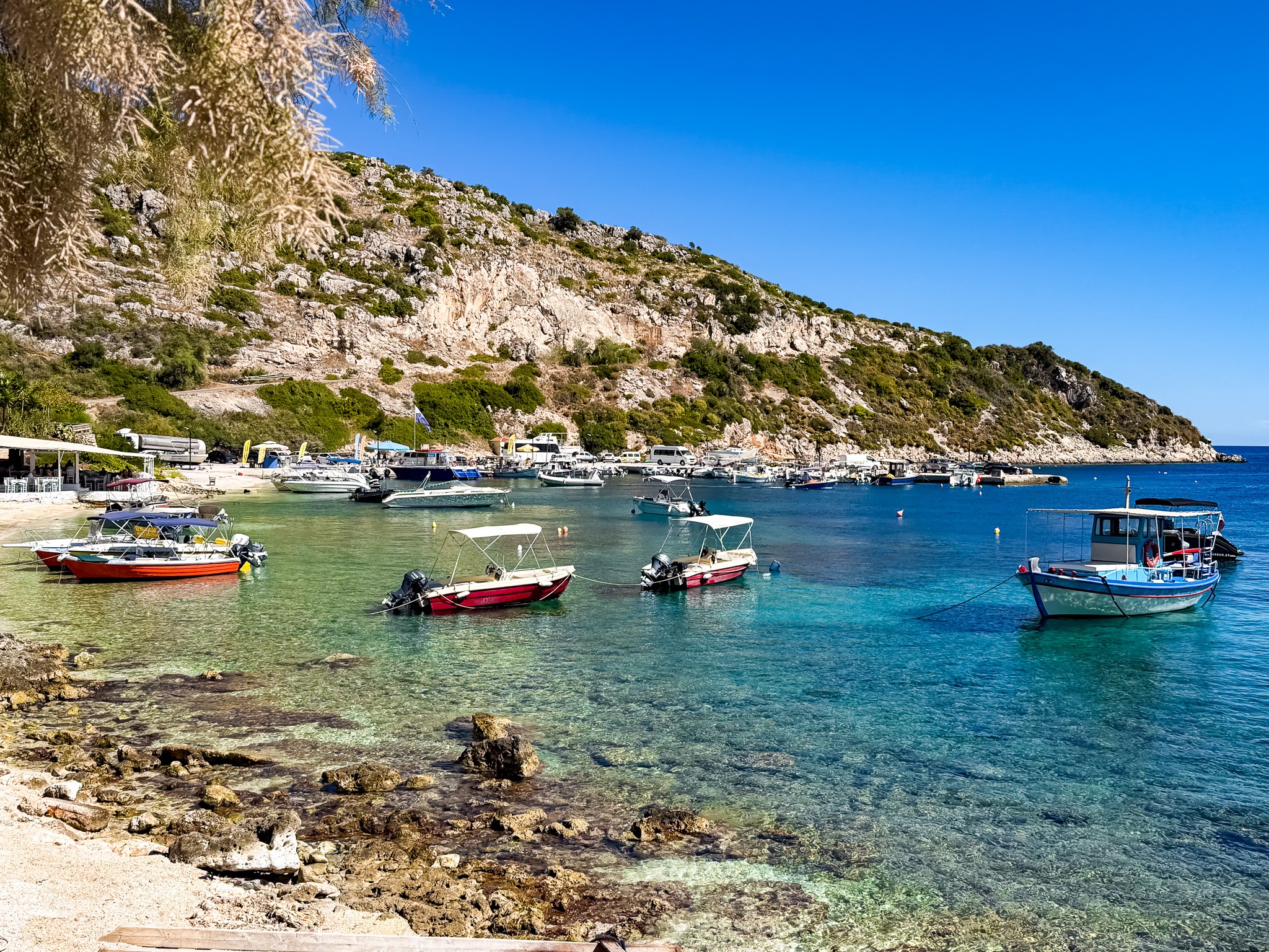 Agios Nikolaos na Zakynthos, mały port z kolorowymi łodziami i turkusową wodą u podnóża skalistych wzgórz