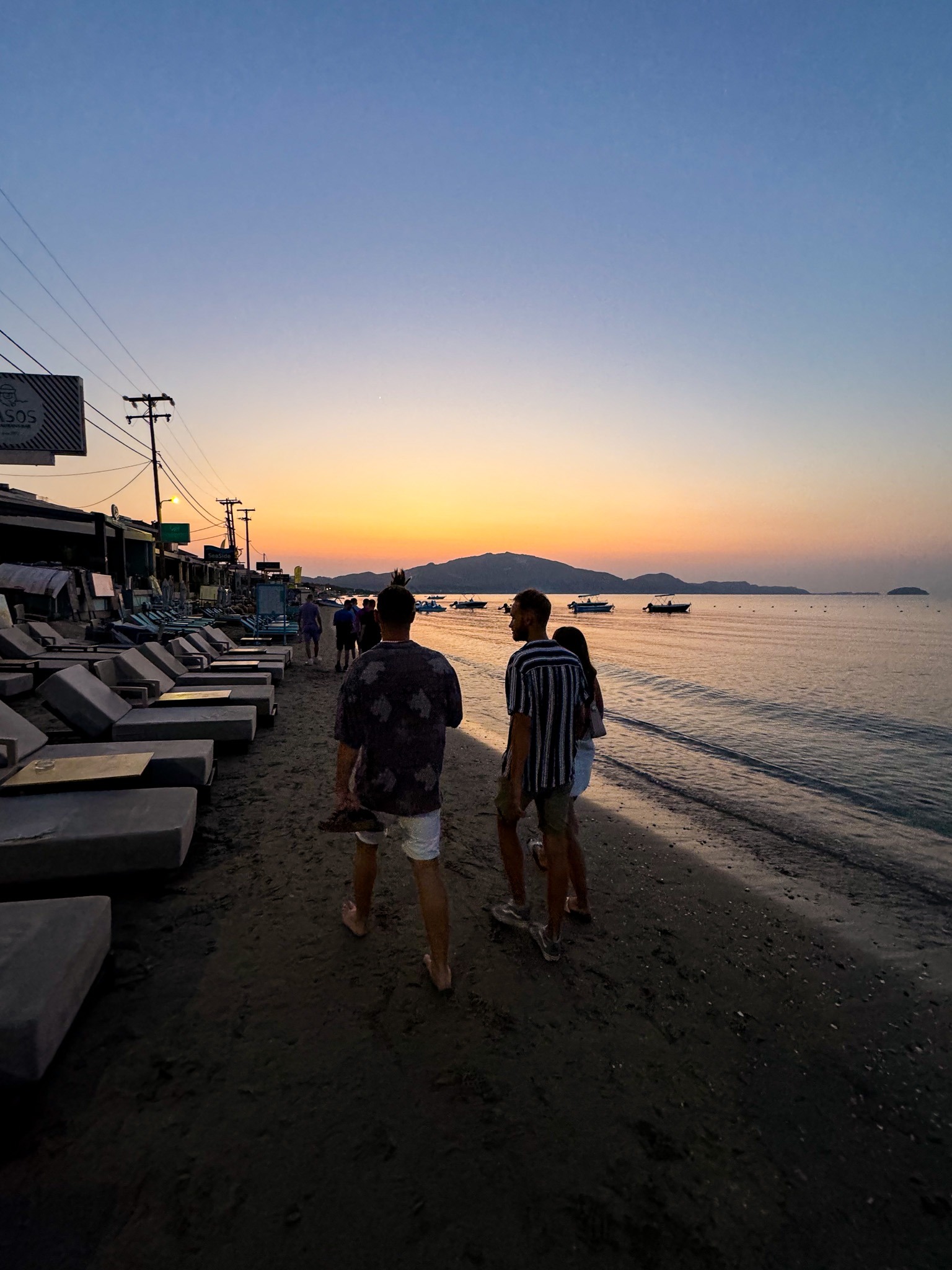 Plaża Laganas na Zakynthos o wschodzie słońca, ludzie spacerujący wzdłuż brzegu morza
