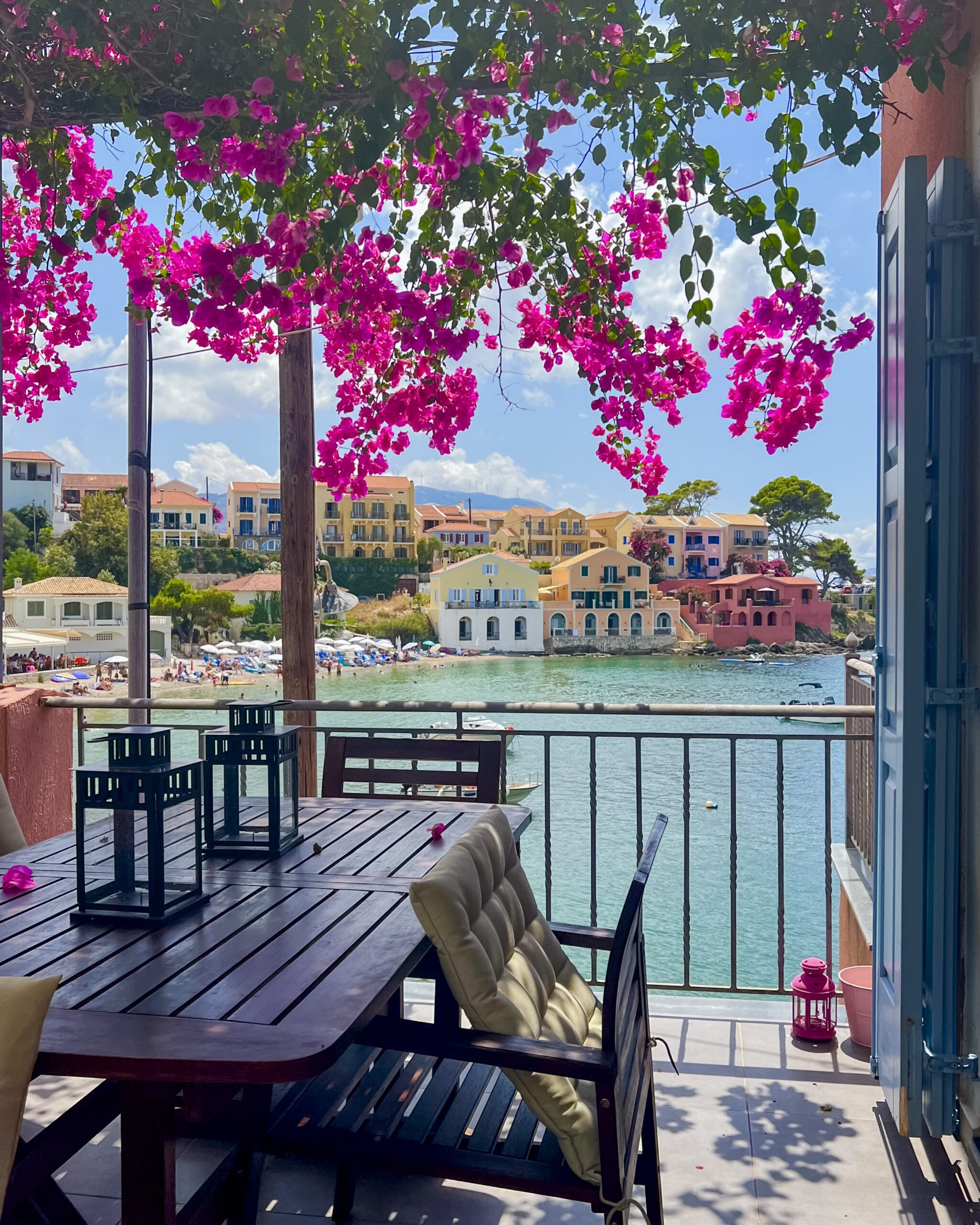 Kolorowe domki w Assos na Kefalonii widziane z tarasu z kwitnącą bugenwillą