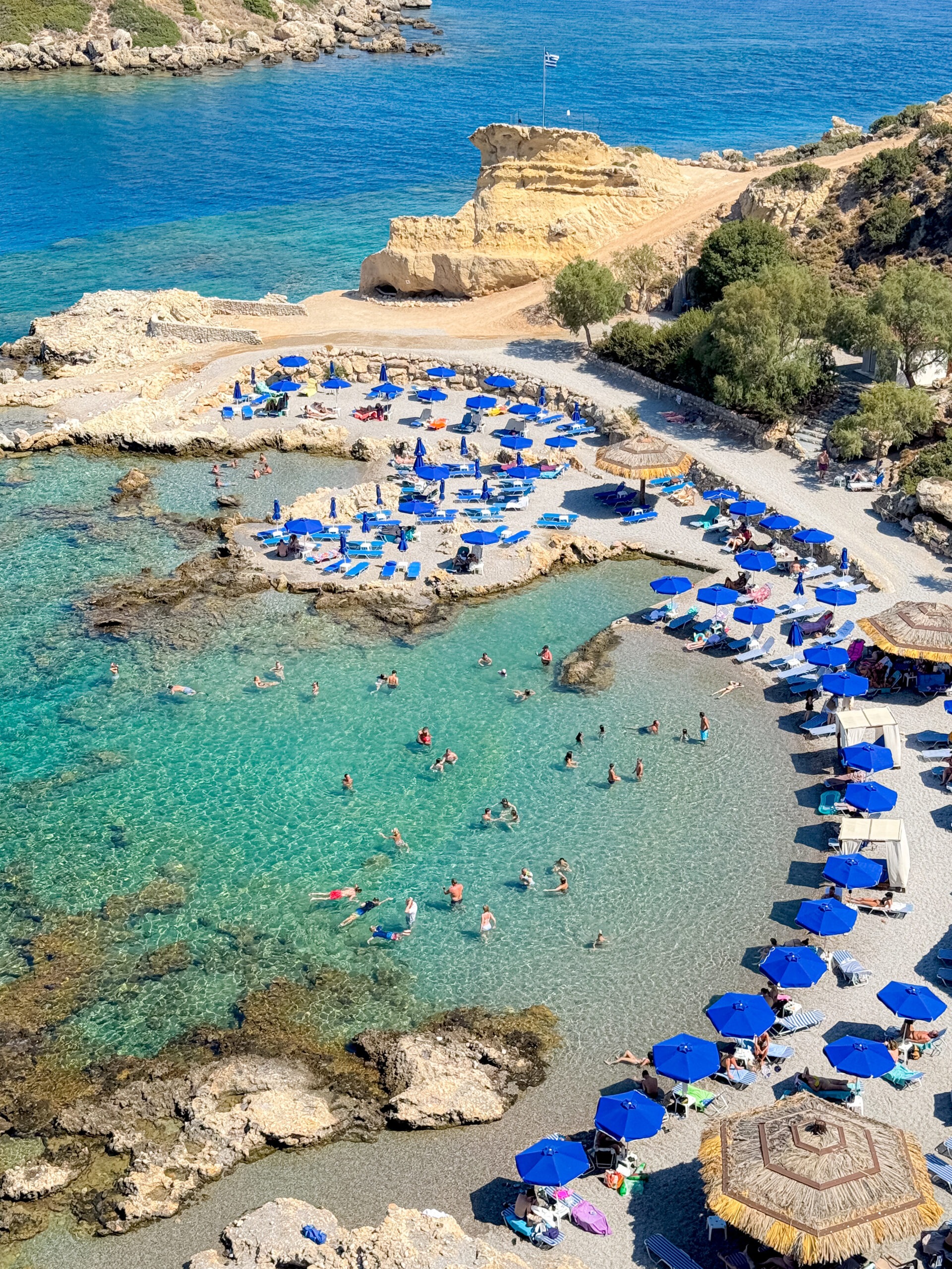 Plaża Grande Blue na Rodos z turkusową wodą, parasolami i kąpiącymi się turystami