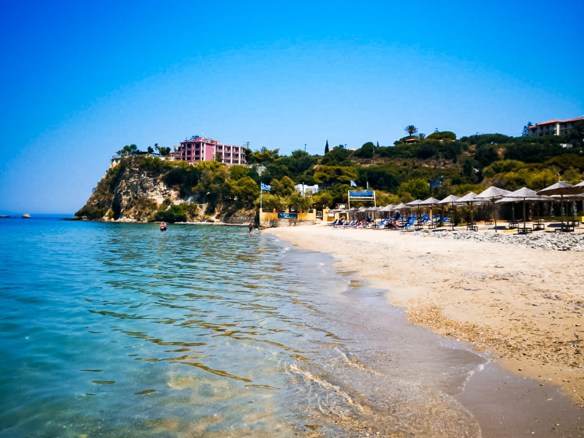 Plaża Tsilivi na Zakynthos z leżakami, parasolami i widokiem na klif oraz turkusowe morze