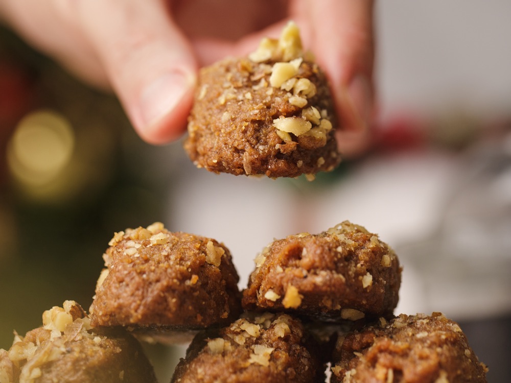 Zbliżenie na greckie ciasteczko Melomakarona trzymane w dłoni, polane miodem i posypane orzechami.