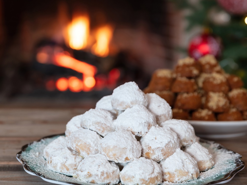 Greckie ciastka Kourabiedes na świątecznym stole, z kominkiem i melomakarona w tle.