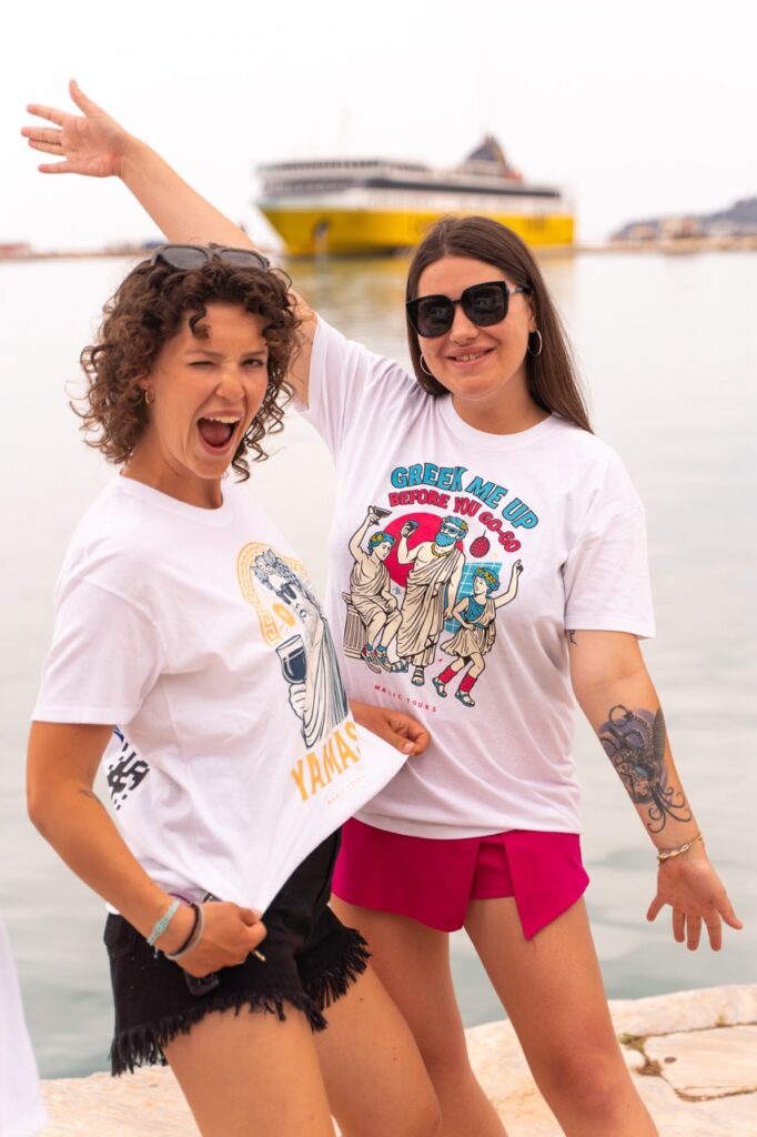 Dwie kobiety w greckich koszulkach Magic Tours – Yamas i Greek Me Up – gadżety i ubrania inspirowane Grecją.