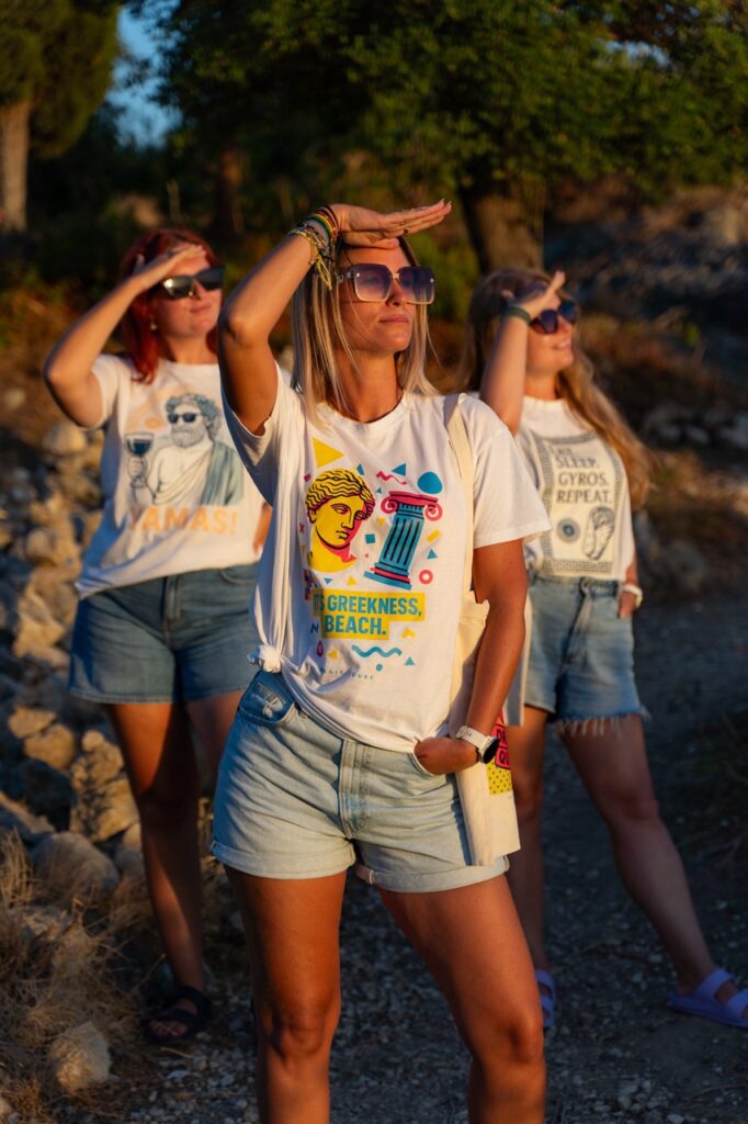 Modelki w koszulkach Magic Tours z greckimi nadrukami na tle zachodu słońca.