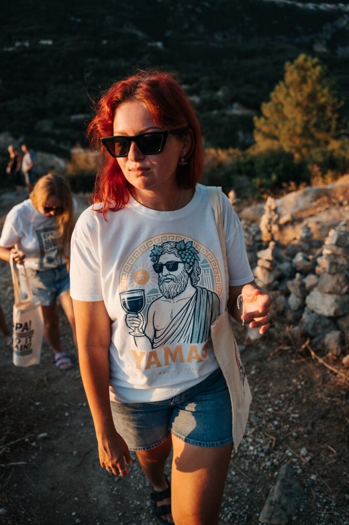 Kobieta w koszulce Yamas Magic Tours podczas spaceru o zachodzie słońca w Grecji.