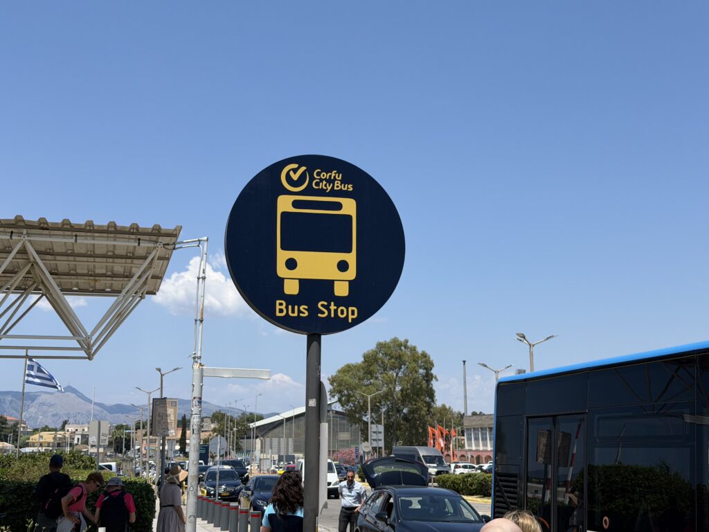 Znak przystanku Corfu City Bus obok niebieskiego autobusu miejskiego na Korfu